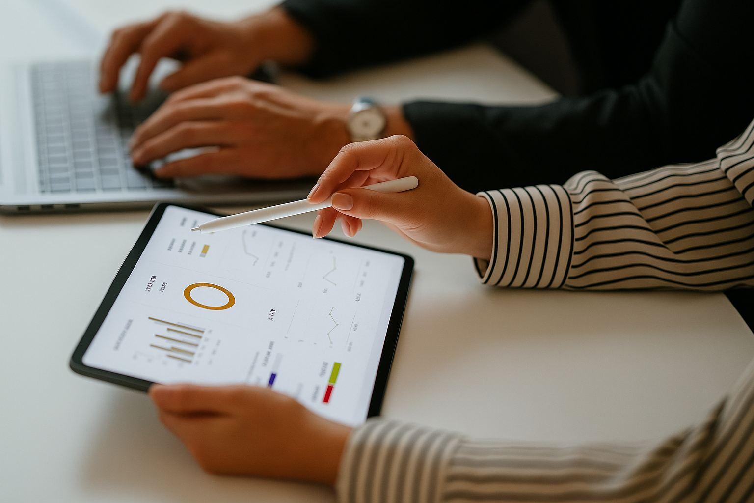 To personer analyserer data på et nettbrett med grafer og diagrammer, mens en laptop er i bruk i bakgrunnen.